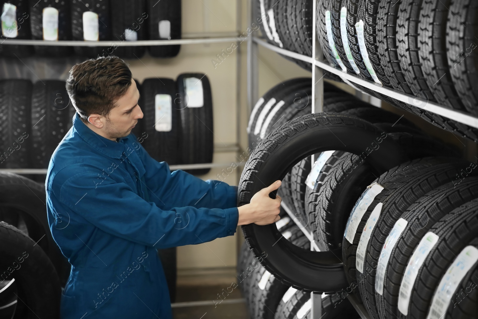 Photo of Young male mechanic with car tires in automobile service center