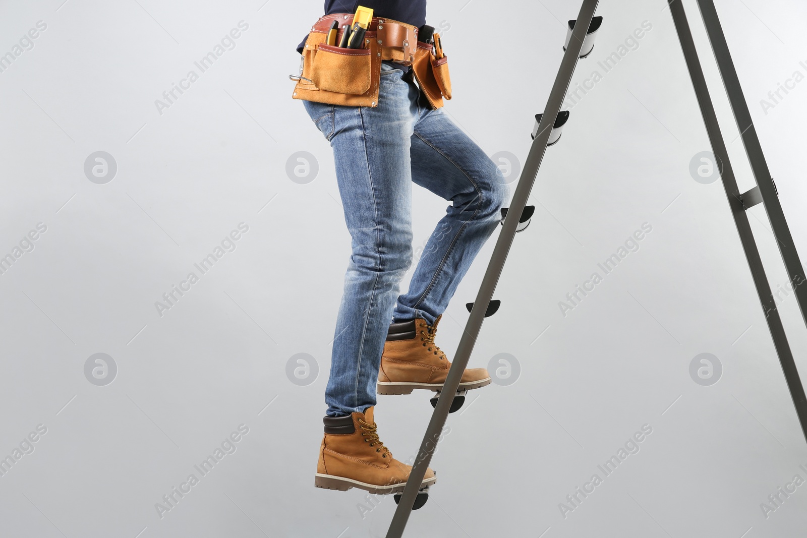 Photo of Professional builder climbing up metal ladder on grey background, closeup of legs