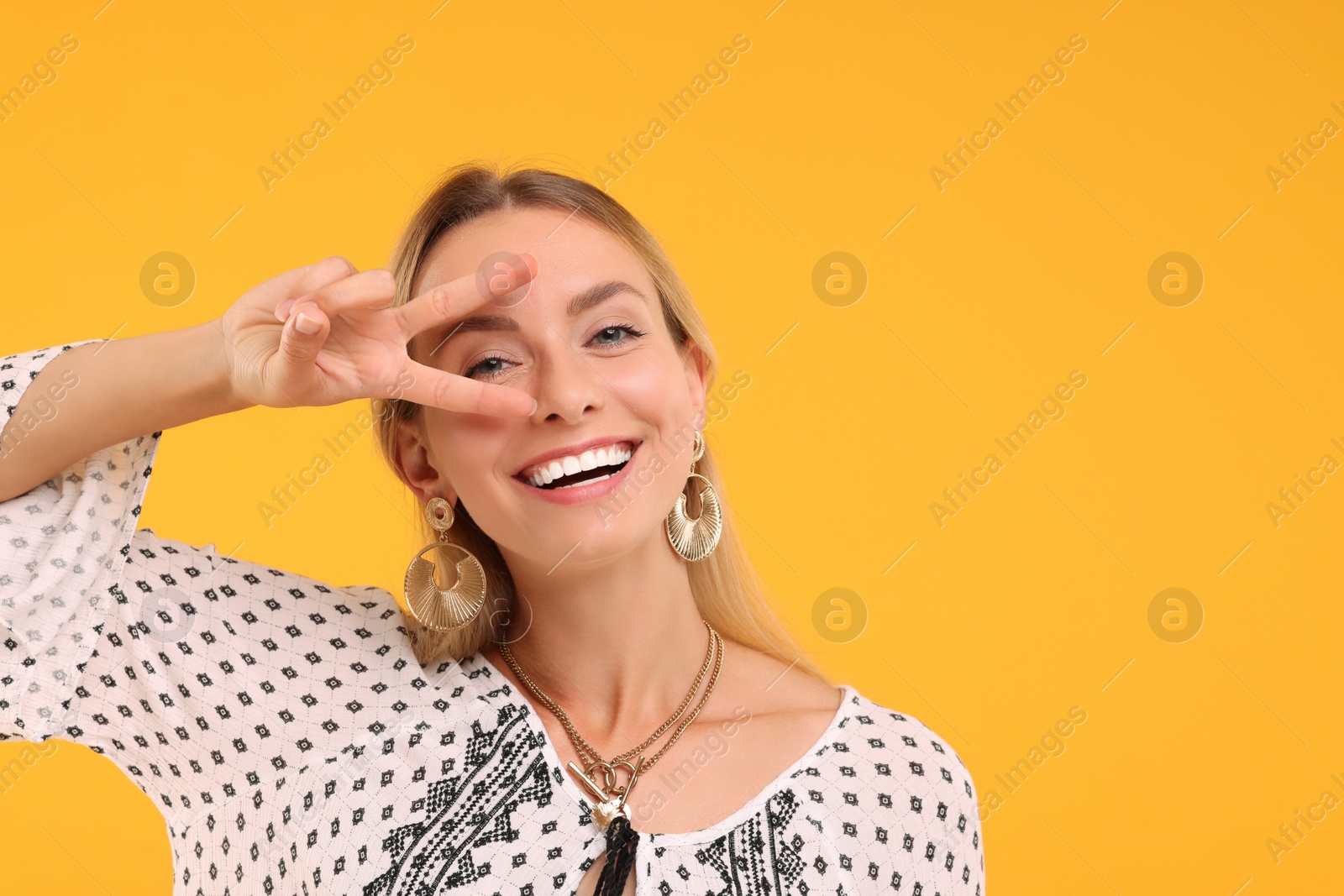 Photo of Portrait of smiling hippie woman showing peace sign on yellow background. Space for text