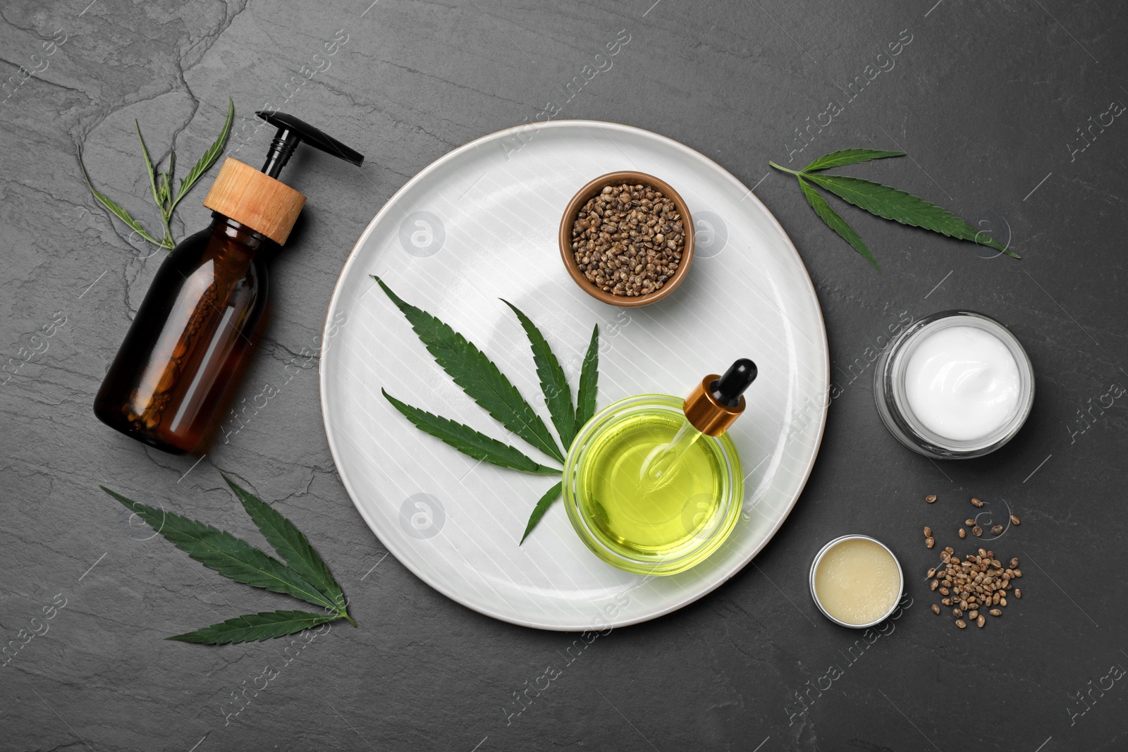 Photo of Hemp cosmetics and green leaves on black table, flat lay