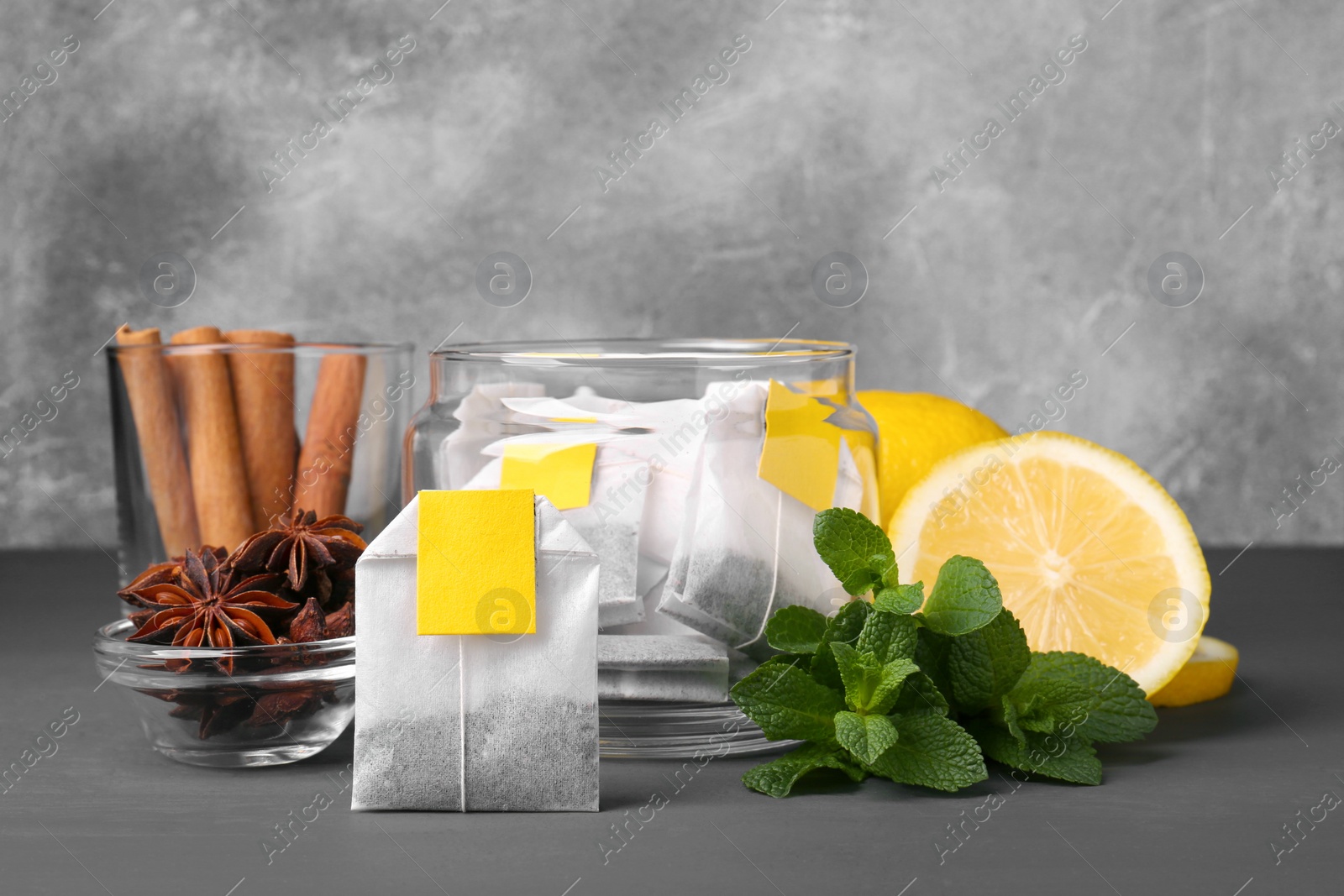 Photo of Tea bags, anise stars, cinnamon sticks, mint and lemon on grey table