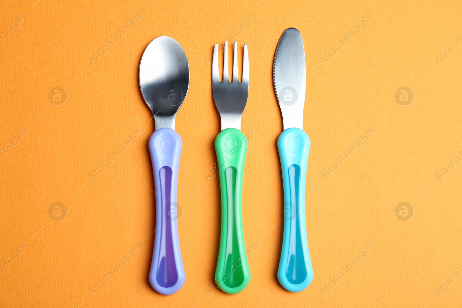 Photo of Set of small cutlery on orange background, flat lay. Serving baby food