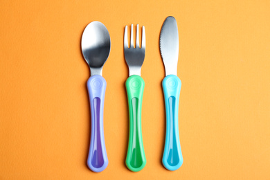 Set of small cutlery on orange background, flat lay. Serving baby food