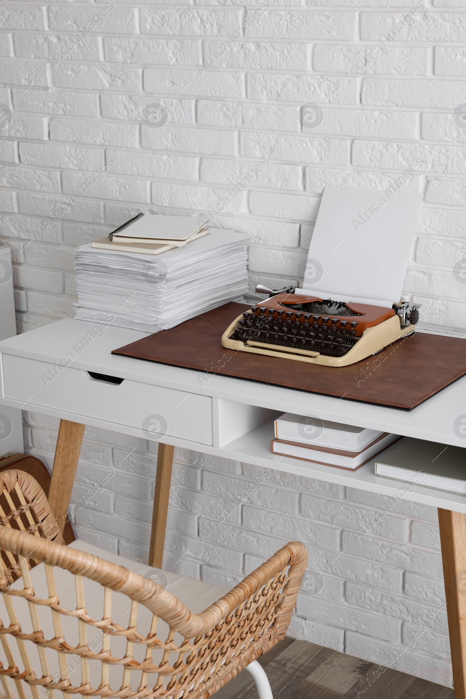 Photo of Comfortable writer's workplace with typewriter on desk near white brick wall