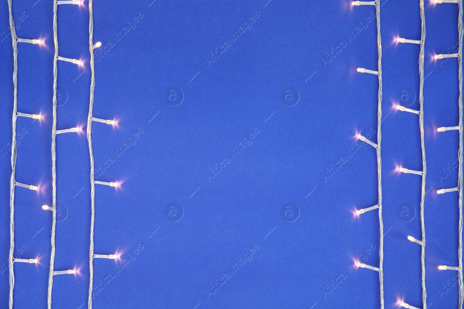 Photo of Glowing Christmas lights on color background, top view