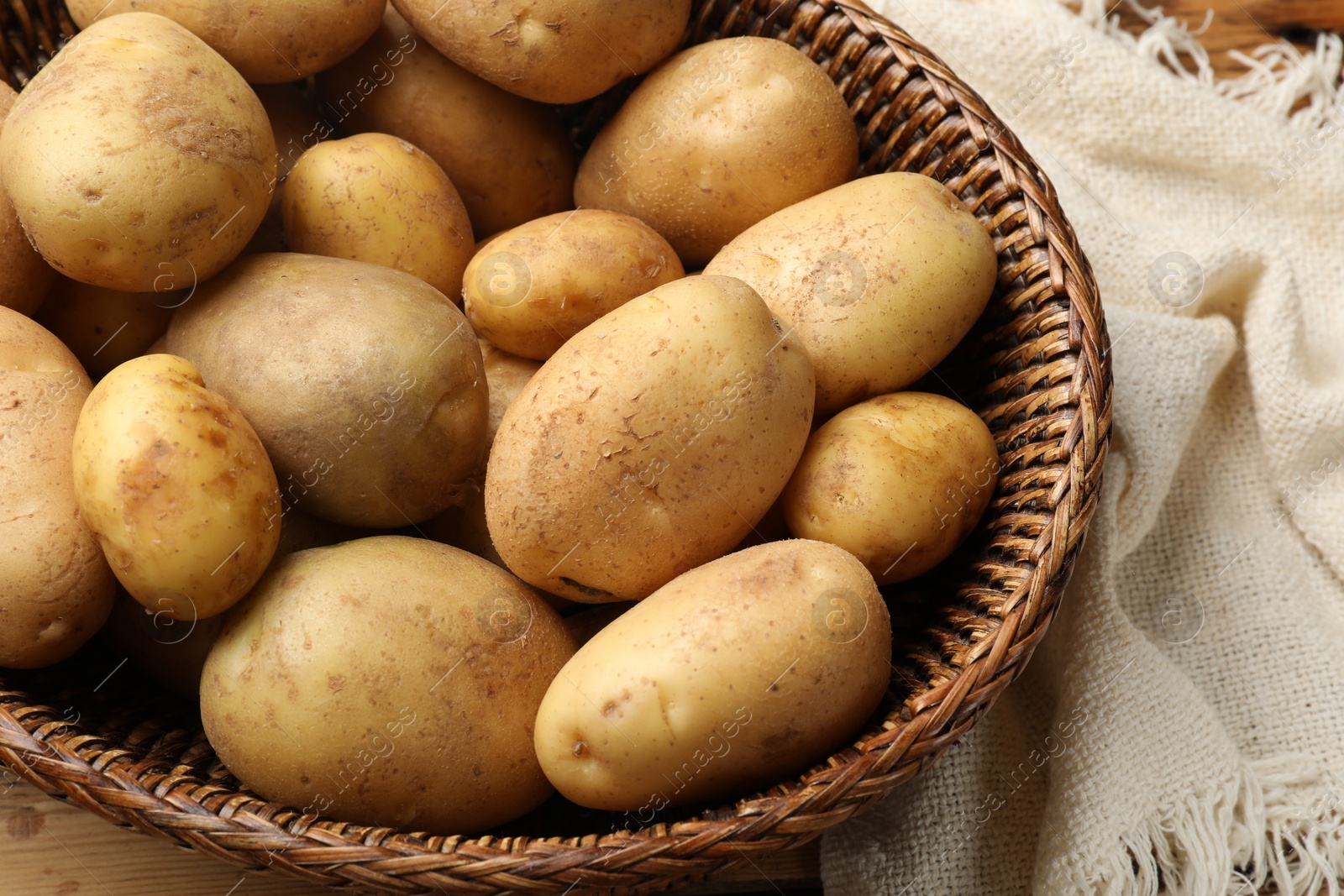 Photo of Raw fresh potatoes in wicker basket on wooden table