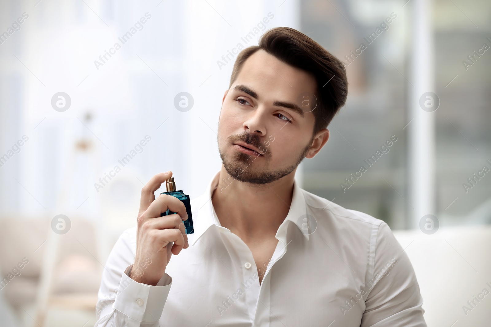 Photo of Handsome man in shirt using perfume on blurred background