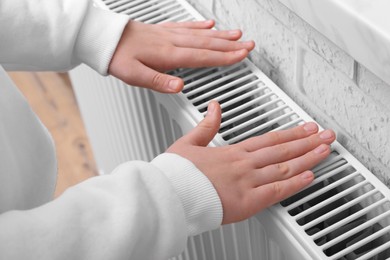 Girl warming hands on heating radiator indoors, closeup