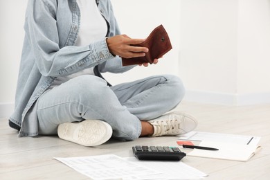 Photo of Woman with empty wallet, credit card and calculator planning budget indoors, closeup. Debt problem