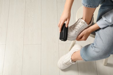 Photo of Woman cleaning stylish footwear indoors, closeup. Shoe care accessory