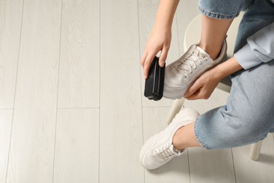 Woman cleaning stylish footwear indoors, closeup. Shoe care accessory