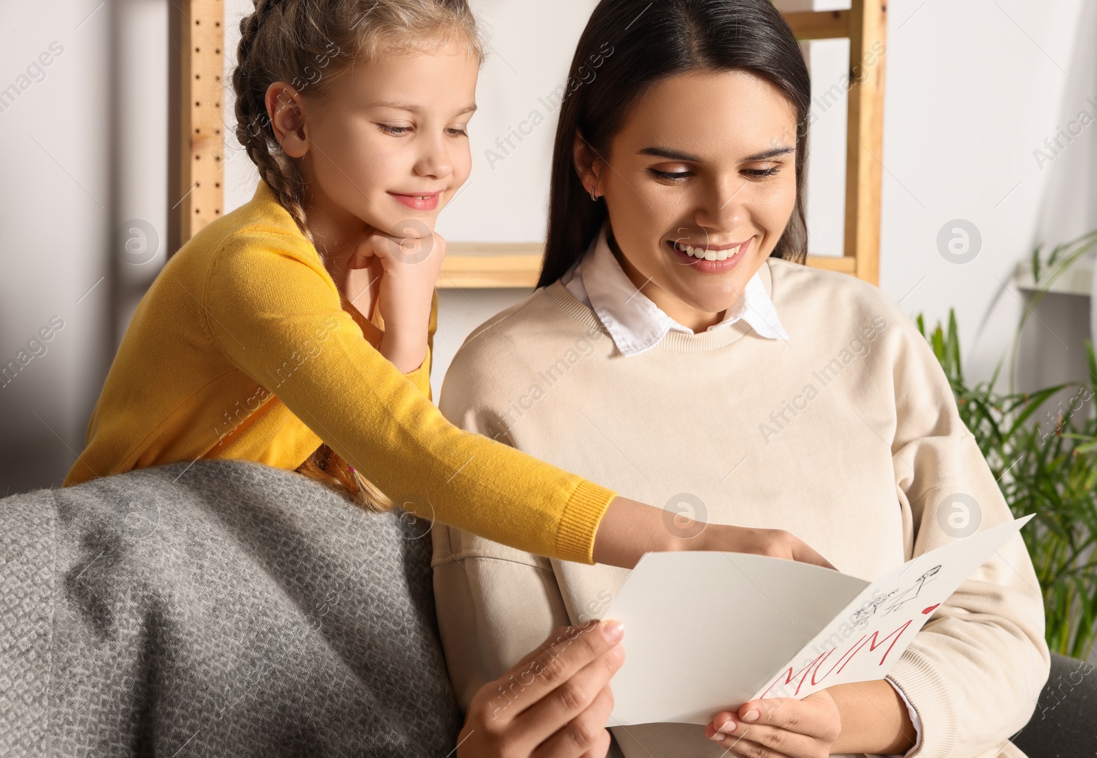 Photo of Happy woman receiving greeting card from her little daughter at home