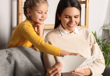 Photo of Happy woman receiving greeting card from her little daughter at home
