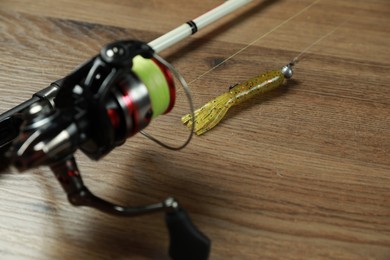 Fishing rod with spinning reel and bait on wooden background, closeup. Space for text