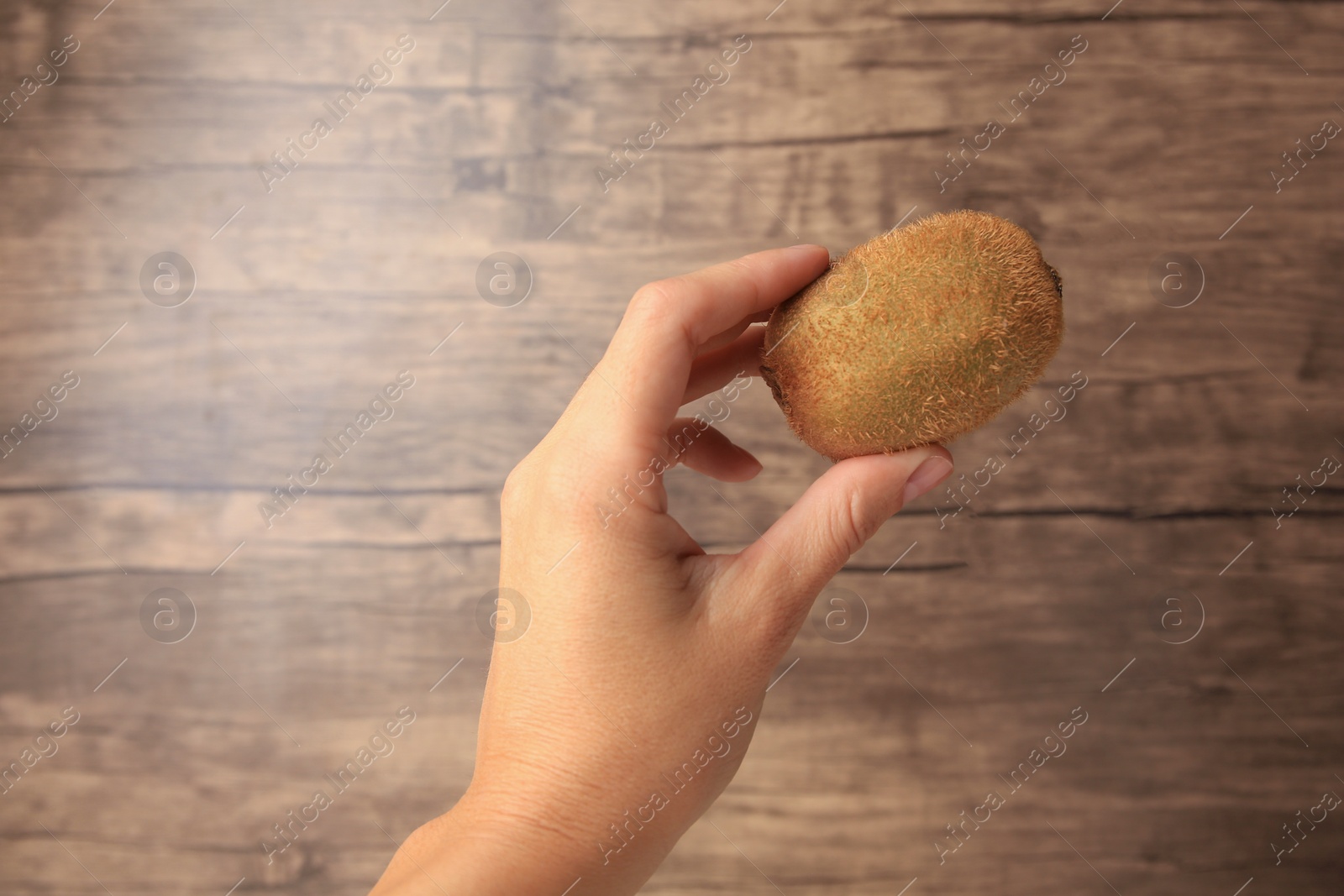 Photo of Woman holding delicious fresh kiwi on wooden background, closeup