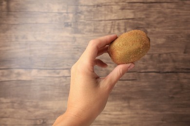 Woman holding delicious fresh kiwi on wooden background, closeup