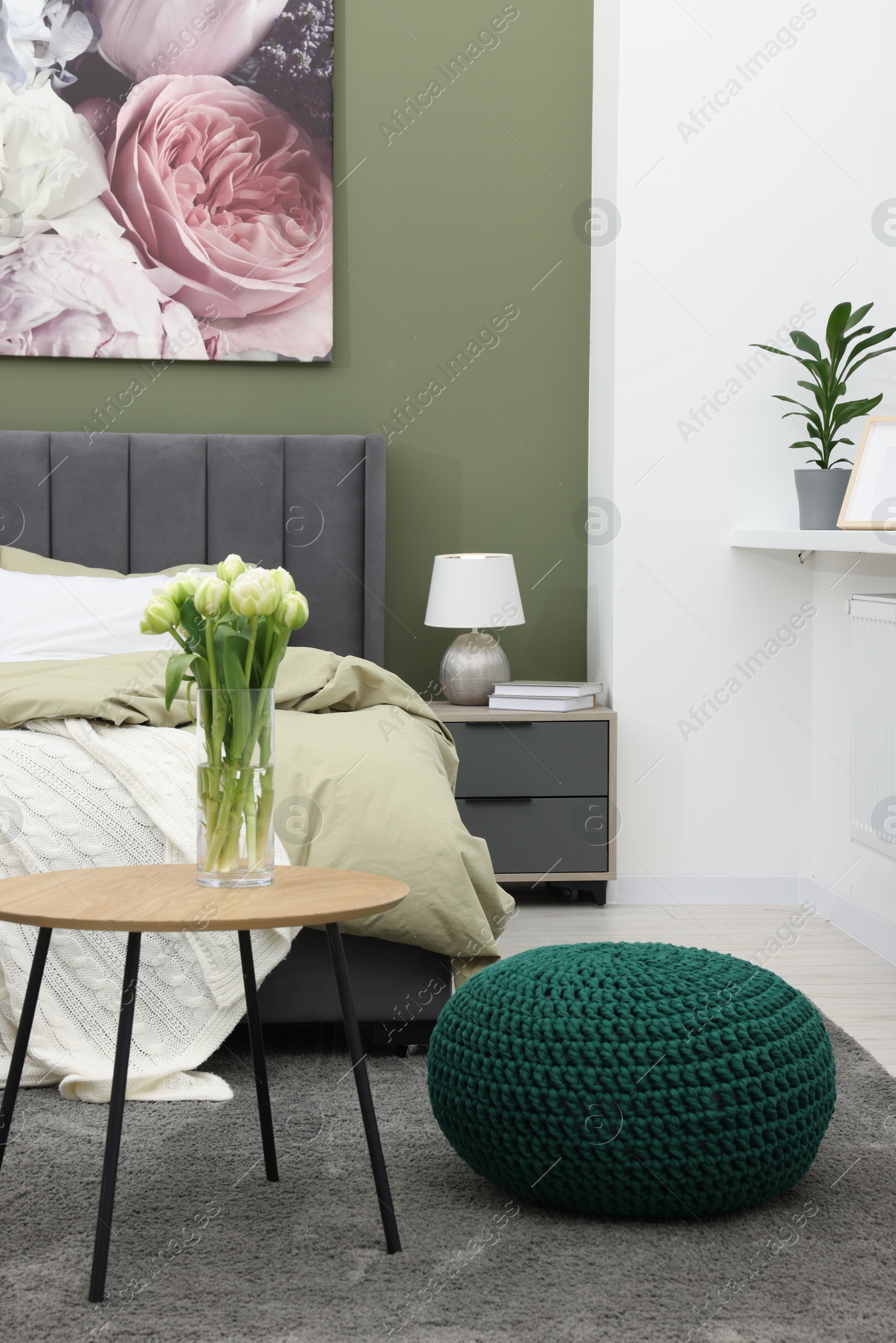 Photo of Stylish bedroom with comfortable bed, bedside table and vase of tulips. Interior design