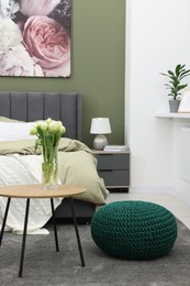 Stylish bedroom with comfortable bed, bedside table and vase of tulips. Interior design