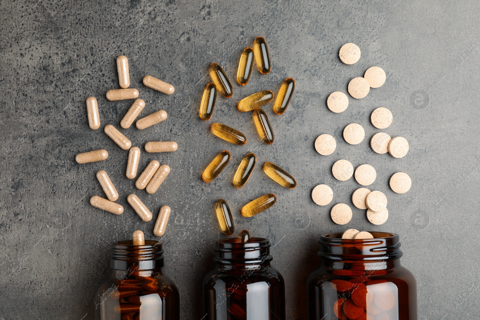 Photo of Overturned bottles with different dietary supplements on grey table, flat lay