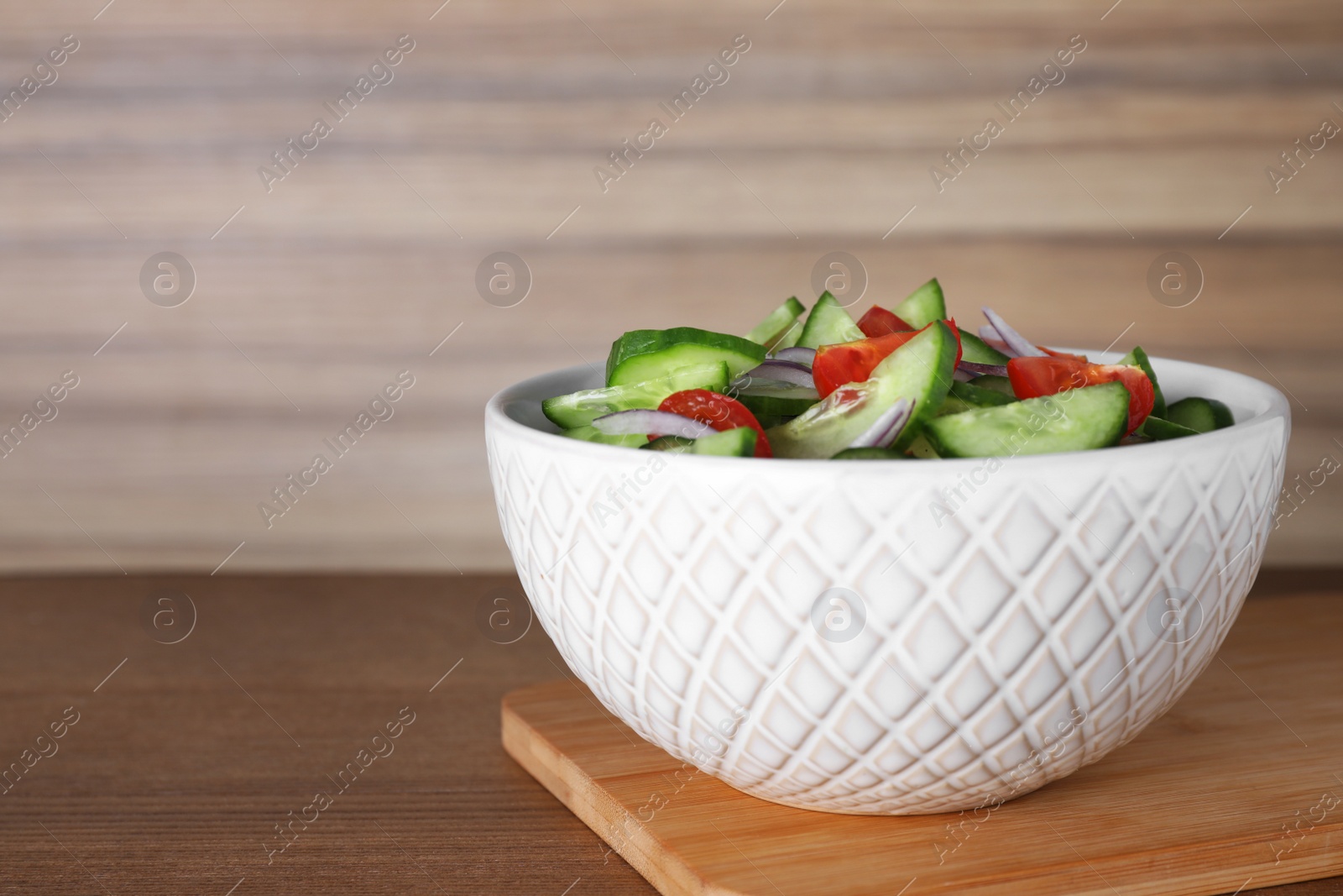 Photo of Bowl of tasty cucumber tomato salad on wooden table. Space for text