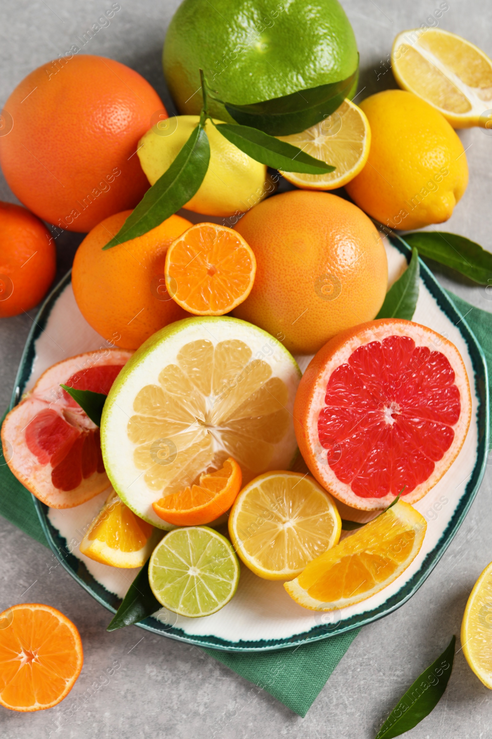 Photo of Different citrus fruits with fresh leaves on light grey table, flat lay