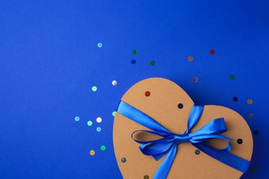 Photo of Beautiful heart shaped gift box with bow and confetti on blue background, top view. Space for text