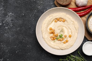 Delicious hummus with chickpeas and different ingredients on black textured table, flat lay. Space for text