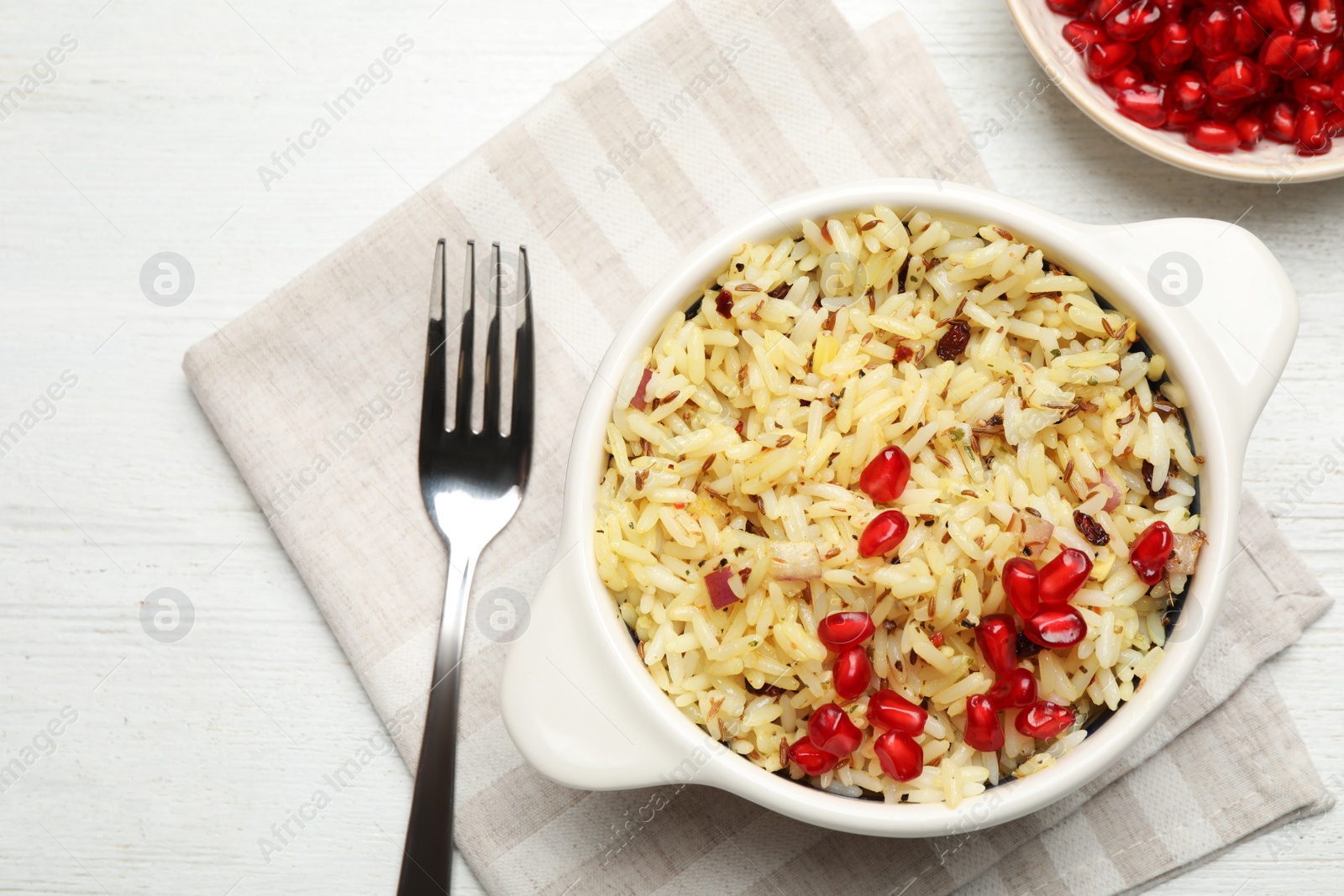 Photo of Tasty rice pilaf with pomegranate grains served on white wooden table, flat lay