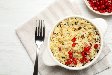 Photo of Tasty rice pilaf with pomegranate grains served on white wooden table, flat lay