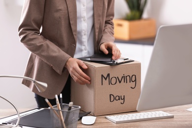 Young woman holding moving box with office stuff indoors, closeup