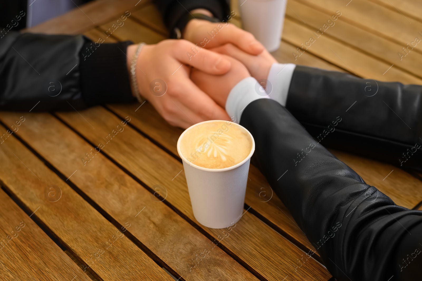 Photo of Lovely couple with coffee holding hands together at wooden table, closeup. Romantic date