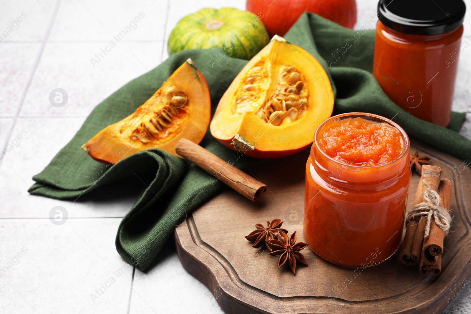 Photo of Jar of delicious pumpkin jam and ingredients on tiled surface