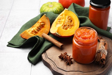 Jar of delicious pumpkin jam and ingredients on tiled surface