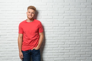 Photo of Young man wearing blank t-shirt near white brick wall. Mockup for design