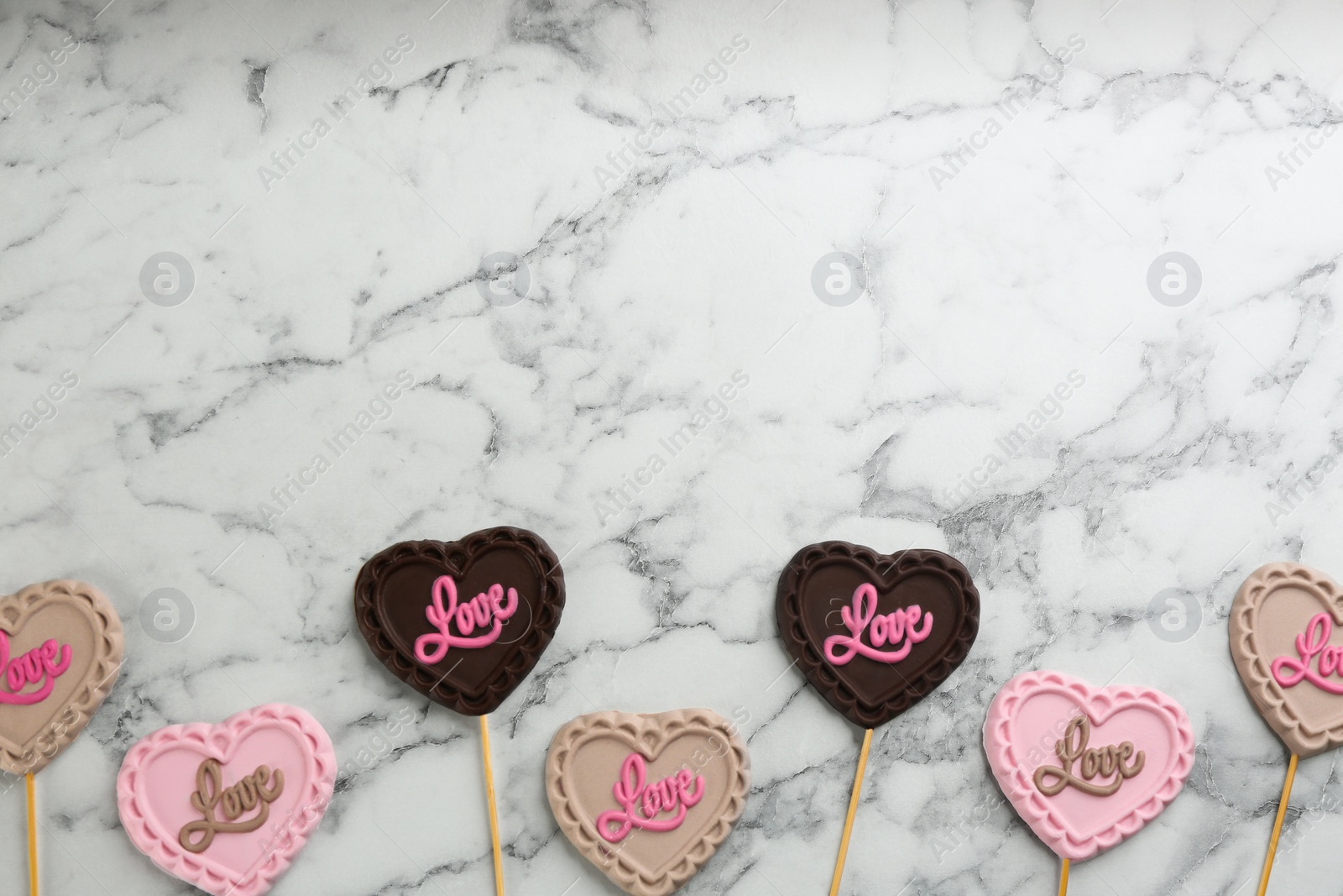 Photo of Different chocolate heart shaped lollipops on white marble table, flat lay. Space for text