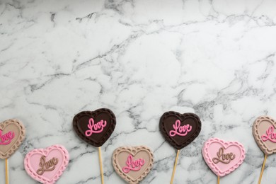 Photo of Different chocolate heart shaped lollipops on white marble table, flat lay. Space for text