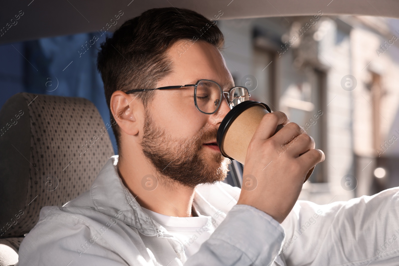 Photo of To-go drink. Handsome man drinking coffee in car