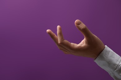 Man holding something in hand on purple background, closeup. Space for text