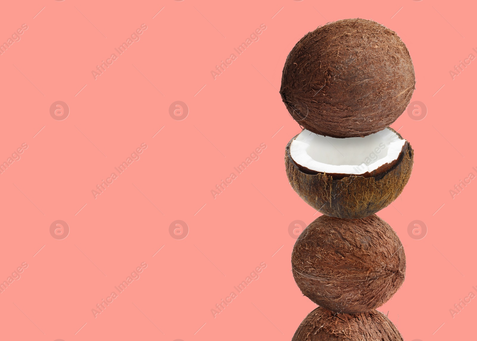 Image of Stack of fresh coconuts on coral color background. Space for text