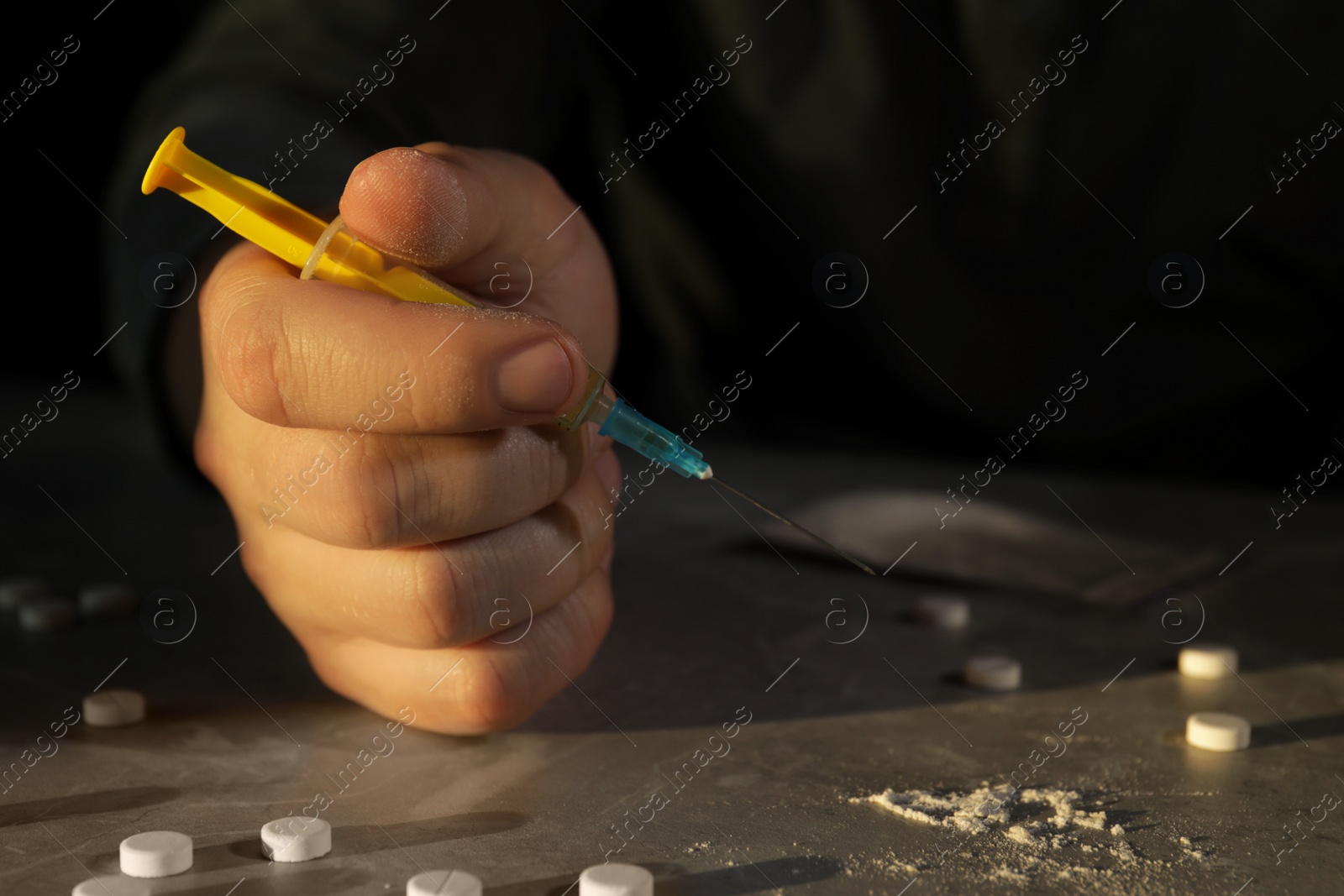 Photo of Addicted man holding syringe near drugs at grey textured table, closeup