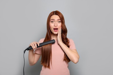 Emotional woman with hair iron on light gray background