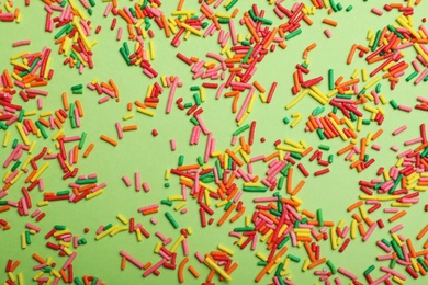 Photo of Colorful sprinkles on green background, flat lay. Confectionery decor