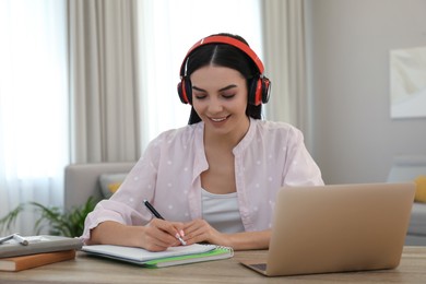 Young woman taking notes during online webinar at table indoors