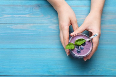 Photo of Woman with tasty blueberry smoothie at light blue wooden table, top view. Space for text