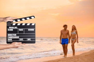 Assistant holding clapperboard and people on beach at sunset, closeup. Cinema production 