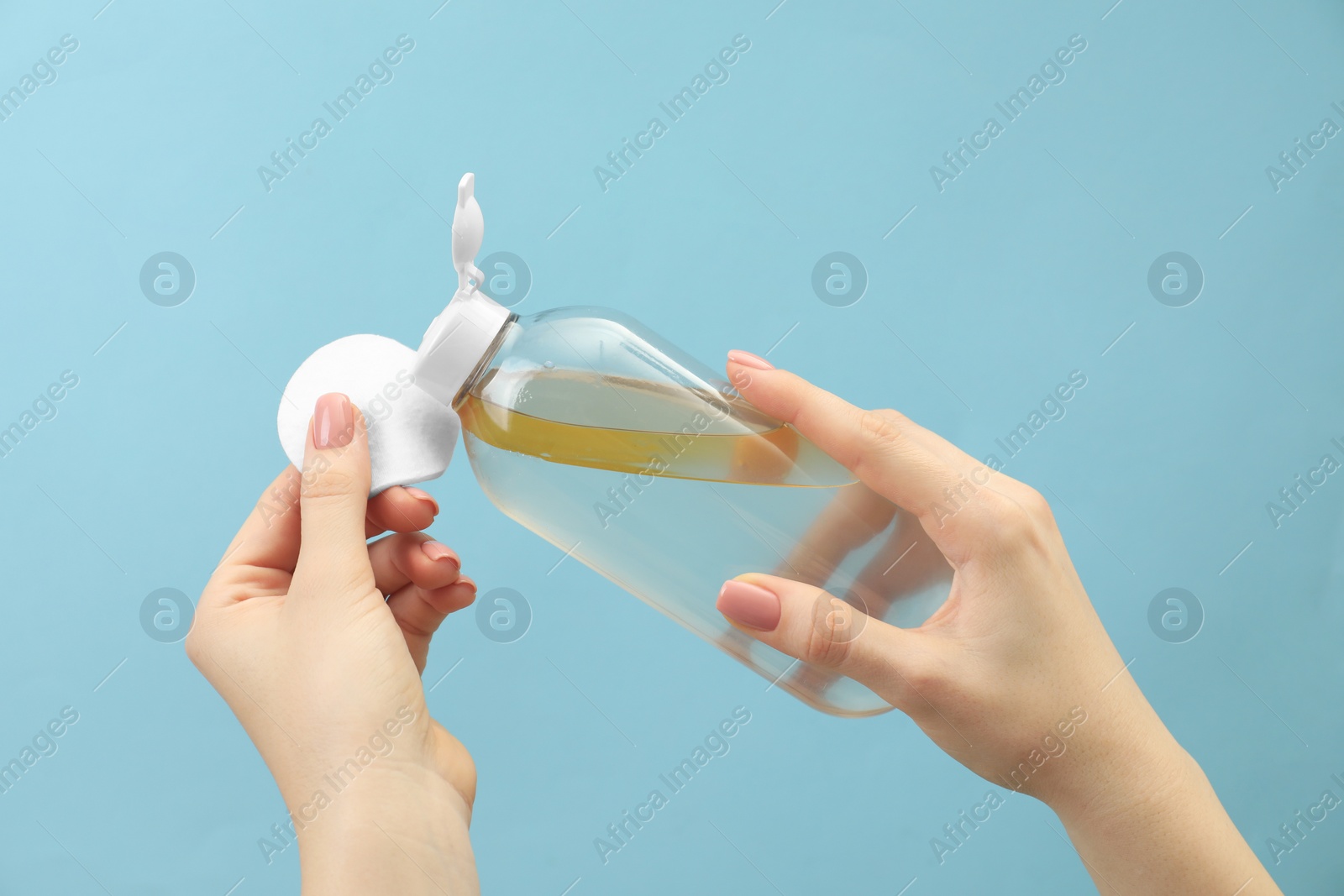 Photo of Woman pouring makeup remover onto cotton pad on light blue background, closeup