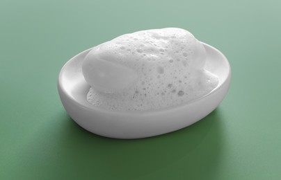 Photo of Dish with soap bar and fluffy foam on green background