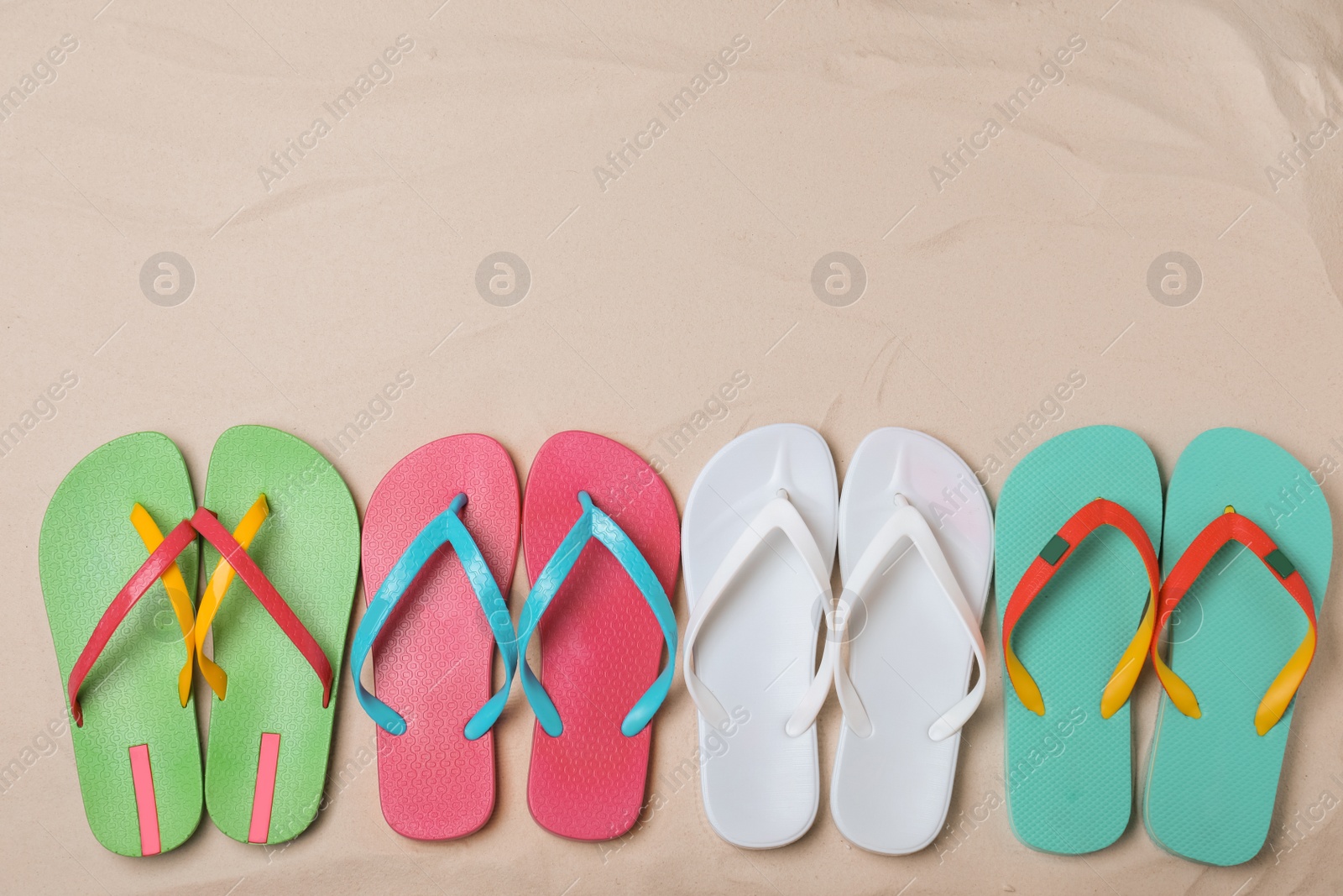 Photo of Different bright flip flops on sand, flat lay. Space for text