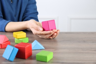 Photo of ABA therapist with colorful building blocks at wooden table, closeup