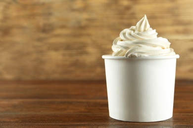 Photo of Cup of tasty frozen yogurt on wooden table. Space for text